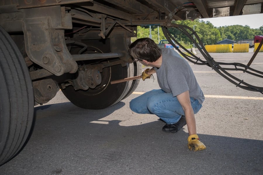 Driver using a tire thumper to check tire pressure on a truck